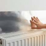 Hand plakt radiatorfolie achter witte radiator, met warme gloed die door de folie wordt teruggekaatst in plaats van de muur